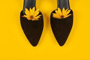 Suede black court shoes with yellow Topinambur flower bud inside toe, yellow background, womanhood photo