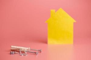 Home repair and redecorated concept. House renovation. Screws and yellow house shaped figure on pink background. photo