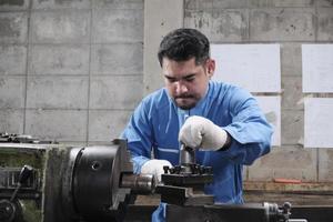One professional Asian male industry engineer worker works in a safety uniform with metalwork precision tools, mechanical lathe machines, and spare parts workshop in the steel manufacturing factory. photo