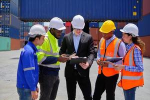 Group of multiracial workers in safety uniforms and hardhats work at logistics terminal dock with stacks of containers, loading control, and management shipping goods, cargo transportation industry. photo