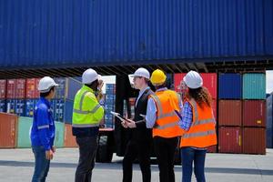 Group of multiracial workers in safety uniforms and hardhats work at logistics terminal dock with stacks of containers, loading control, and management shipping goods, cargo transportation industry. photo