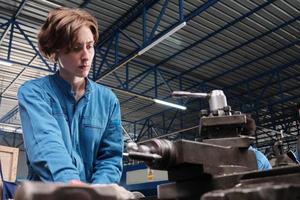 Professional young White female industry engineer worker works in safety uniform with metalwork precision tools, mechanical lathe machines, and spare parts workshop in the steel manufacturing factory.