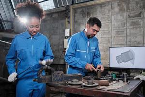 dos trabajadores profesionales de ingeniería de la industria se asocian en trabajos de metalurgia de uniformes de seguridad con dibujo mecánico en un monitor, herramientas de máquinas de torno y taller de piezas de producción en la fábrica de fabricación. foto