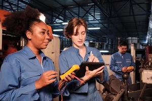 dos ingenieras profesionales con uniformes de seguridad trabajan inspeccionando la corriente de voltaje de las máquinas, comprobando y manteniendo en la fábrica de fabricación, ocupaciones de servicio del sistema eléctrico. foto