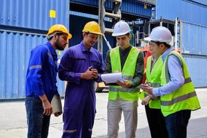 A Group of multiracial workers people in safety uniforms and hardhats work at logistics terminal with many stacks of containers, loading control shipping goods for the cargo transportation industry. photo