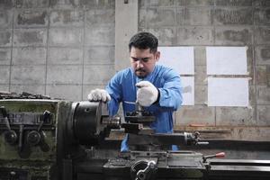 One professional Asian male industry engineer worker works in a safety uniform with metalwork precision tools, mechanical lathe machines, and spare parts workshop in the steel manufacturing factory. photo