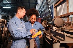 Asian male and female African American engineers in safety uniform work by inspecting machines' voltage current, checking, and maintaining at manufacture factory, electric system service occupations. photo