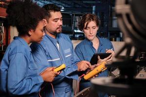 Los equipos multirraciales de ingenieros de la industria profesional con uniformes de seguridad trabajan inspeccionando la corriente de voltaje de las máquinas, comprobando y manteniendo en la fábrica de fabricación, ocupaciones de servicio del sistema eléctrico. foto