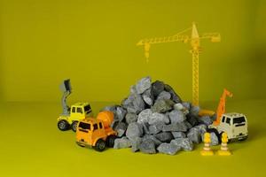 Models simulator on yellow background, construction vehicles toys, trucks, backhoes, and cranes site work, transport resource materials, rock, stone, and mortar, built real estate development business photo