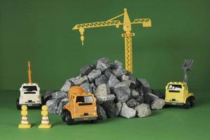 Models simulator on green background, construction vehicles toys, trucks, backhoes, and cranes work at site, transport resource materials, rock, and mortar, real estate business, and city development. photo