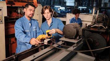 Asian male and White female engineer workers in safety uniforms work by inspecting machines' voltage current, checking, and maintaining at manufacturing factory, electric system service occupations. photo