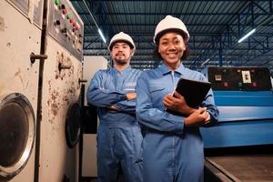 retrato de dos ingenieros profesionales de la industria asociados con cascos y uniformes de seguridad mirando la cámara y sonriendo, inspeccionando y manteniendo la máquina de control en la fábrica de fabricación, ocupación de servicio. foto