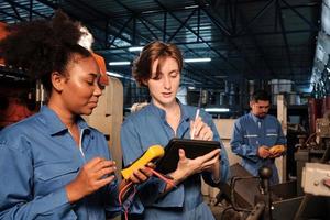 dos ingenieras profesionales con uniformes de seguridad trabajan inspeccionando la corriente de voltaje de las máquinas, comprobando y manteniendo en la fábrica de fabricación, ocupaciones de servicio del sistema eléctrico. foto