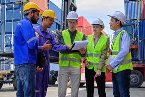 A Group of multiracial workers people in safety uniforms and hardhats work at logistics terminal with many stacks of containers, loading control shipping goods for the cargo transportation industry. photo