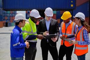 Group of multiracial workers in safety uniforms and hardhats work at logistics terminal dock with stacks of containers, loading control, and management shipping goods, cargo transportation industry. photo