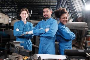 Multiracial industry workers in safety uniforms collaborate with unity, arms crossed, and express happy work together with smile and cheerful in mechanical factory, professional engineer occupation. photo