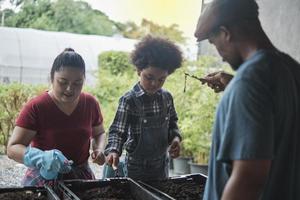 familia de granjeros afroamericanos enseña a su hijo a preparar biofertilizantes juntos con lombrices de tierra en el suelo, aprendizaje de biología y ecología natural, pasatiempo de jardinero orgánico, agricultura rural infantil. foto