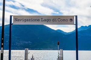 Stock photo of ferry pier and ferry sign, lake Como, Lombardy, Italy. Sign reads Navigazione Lago di Como. This pier is in Menaggio. It is a beautiful sunny summer day