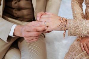 The groom is wearing a wedding ring to the bride during the engagement ceremony. According to the tradition of Thailand, the bride wears a traditional Thai dress. photo