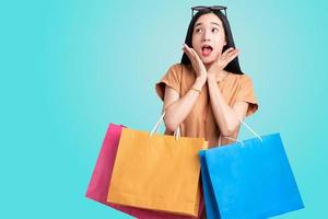 retrato de una mujer asiática que lleva bolsas de compras coloridas en un fondo azul aislado, concepto de venta de verano, una mujer joven disfruta feliz con las compras foto