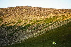 Green tent stand by mountains on sunset outdoors. Solitude in nature concept photo