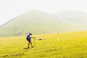 Side view fit sporty female hiker with nordic walk sticks go uphill in green hiking trail in caucasus mountains .Recreational activities and healthy lifestyle concept photo