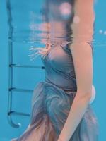 surreal art portrait of young woman in grey dress and beaded scarf underwater in the swimming pool photo