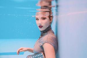 surreal art portrait of young woman in grey dress, beaded scarf, small bag, violet high heels  underwater in the swimming pool photo