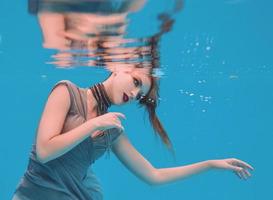 surreal art portrait of young woman in grey dress and beaded scarf underwater in the swimming pool photo