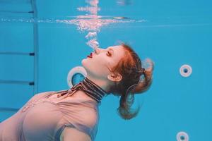 surreal art portrait of young woman in grey dress and beaded scarf underwater in the swimming pool photo