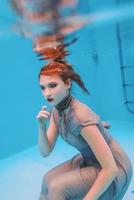 surreal art portrait of young woman in grey dress and beaded scarf underwater in the swimming pool photo