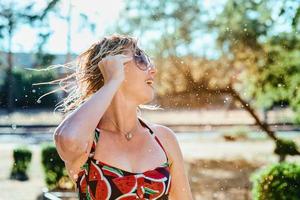 risa emocional mujer rubia con el pelo mojado haciendo salpicaduras de agua. vacaciones, felicidad, diversión, verano, concepto de ocio. foto