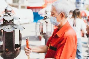 Portrait image adult 60 years old. Elderly man wearing mask to protect against toxic dust pm2.5 or virus, lighting red candle. The white-haired man is about to make wish. People wear red shirts. photo