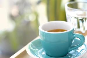 Cup of black hot coffee on a table in cafe with steam and morning sunlight. photo