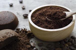 ground coffee in a wooden bowl on concrete background with a pile of arabica coffee beans. photo