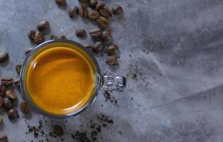 espresso caliente en una taza de vidrio sobre una mesa de concreto con un montón de granos de café arábica asados. foto