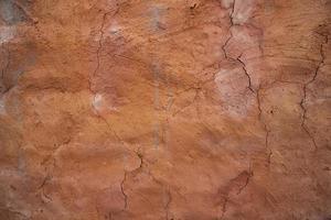 The texture of a red concrete wall with cracks and scratches can be used as a background photo