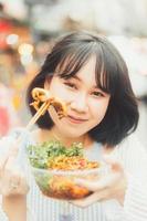joven mujer asiática adulta comiendo comida de calamar picante a la parrilla en el mercado de Chinatown del sudeste asiático foto