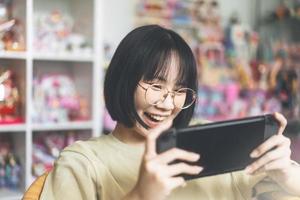 estilo nerd feliz joven adulto jugador asiático mujer usar anteojos jugar un juego en línea foto