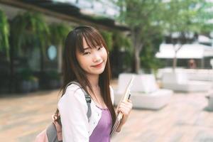 Portrait of young adult asian college student woman with notebook on day in the city. photo