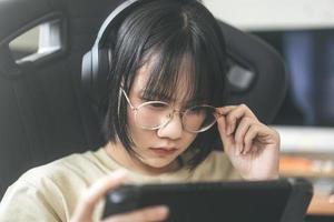 Una joven jugadora asiática de estilo nerd usa anteojos y auriculares para jugar un juego en línea foto