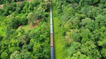 Drone footage of a diesel locomotive passenger train on a rural railroad track moving through a lush tropical forest during the rainy season. video