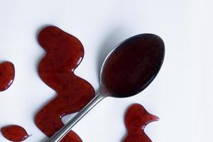 las gotas de salsa casera y una cuchara sobre un fondo blanco foto
