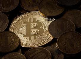 The shiny golden bitcoin is half-filled with old coins. Bitcoin against the background of old coins. photo