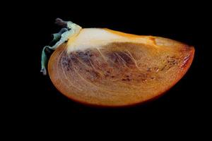 A slice of ripe persimmon is isolated on a black background. photo