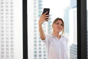 Portrait of a young attractive woman making selfie photo on smartphone in modern office building background