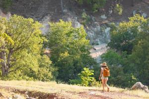 girl traveler with a backpack goes along a mountain path. photo