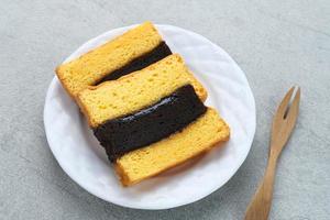 Spiku or Lapis Surabaya or Surabaya Layer Cake is a three-layer sponge cake with strawberry jam in between. Served in white plate, close up. photo