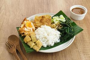 Nasi Pecel, a traditional Javanese rice with vegetable salad and peanut sauce, served with side dishes such as egg, martabak, and peyek crackers. photo