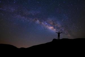 paisaje con vía láctea, cielo nocturno con estrellas y silueta de gente feliz parada en la montaña, fotografía de larga exposición, con grano foto